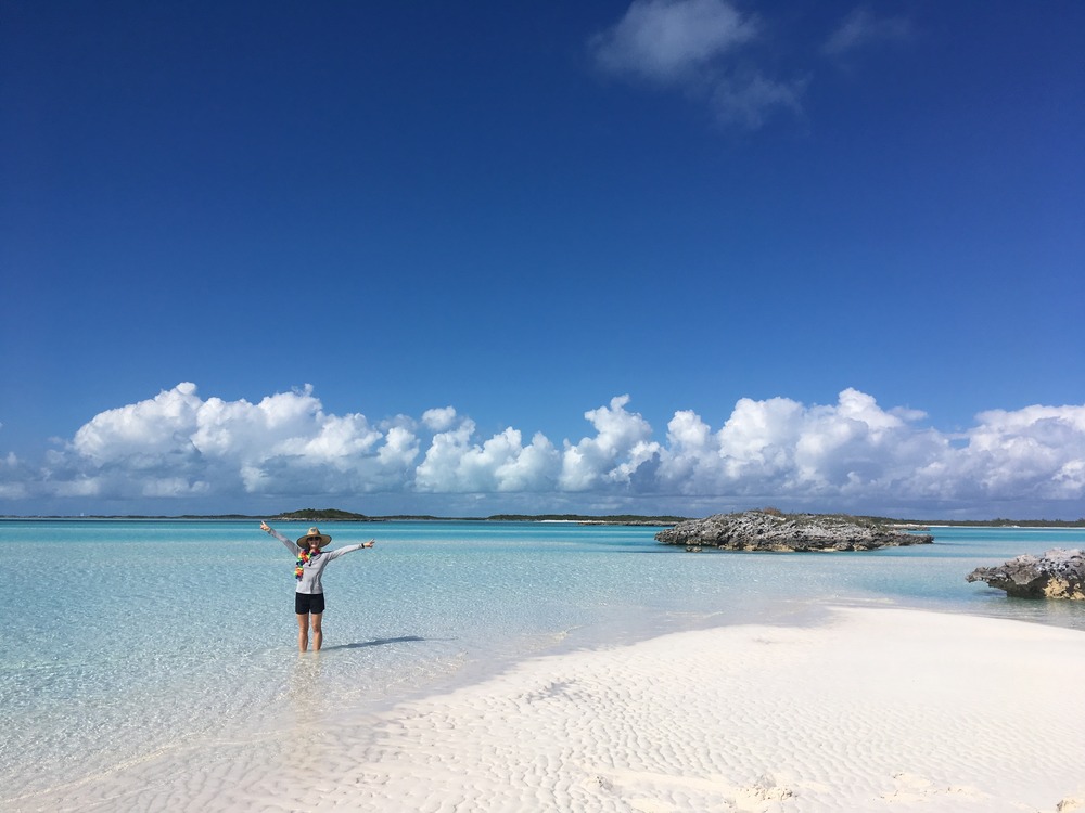 woman standing on a perfect white sand beach with crystal clear blue water in the Bahamas